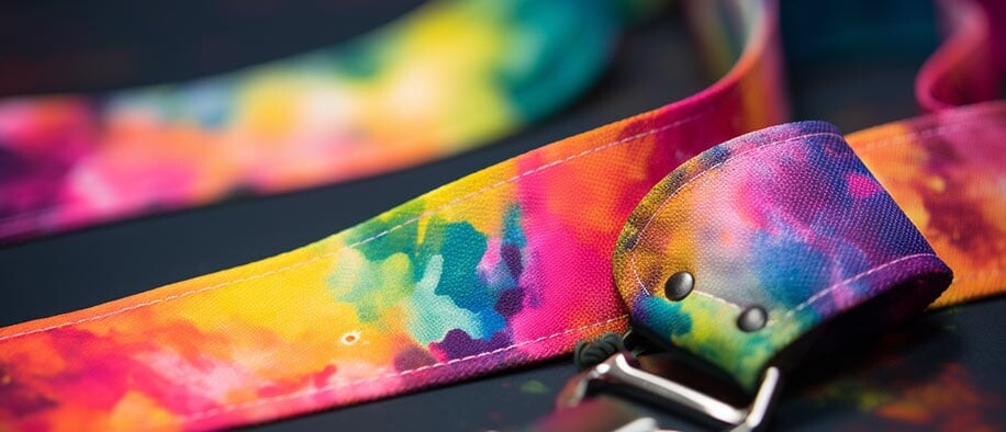 Close-up of a tie-dye rainbow lanyard with a riveted loop and metal clip, on a dark surface