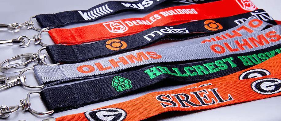 Black, red, gray and orange woven lanyards with stitched logos and silver hooks on a gray surface